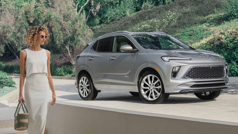 Fashionable Woman Walking From Parked Buick Encore GX Avenir in Driveway